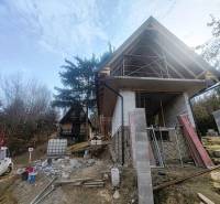 Eine Hütte im Bau auf Zajačia Debra in Holčíkovce, umgeben von Bäumen und Baumaterial.