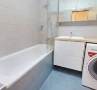 Badezimmer mit Badewanne, Waschbecken, Spiegel und Waschmaschine in einer 3-Zimmer-Wohnung.