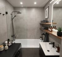 Stilvolles Badezimmer in einer 3-Zimmer-Wohnung mit Badewanne, Dusche, Regalen und beleuchtetem Spiegel.