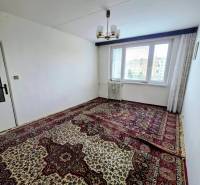 Ein Zimmer einer 3-Zimmer-Wohnung mit Teppich und Kronleuchter, helle Wände, Heizkörper unter dem Fenster.