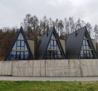 Häuser in der Straße Evy in Holčíkovce mit dreieckigem Dach, umgeben von Natur und Wald.