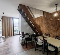 Eine Hütte mit einem Boden in Holzoptik, einer Treppe und einem Tisch neben einer Wand aus Holzlamellen.