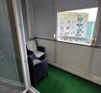 Balkon in einer 3-Zimmer-Wohnung mit einem Rattansessel und einem grünen Teppich.