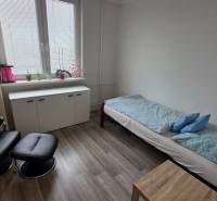 Ein Zimmer mit einem Sessel, einem Bett und einem Schrank, ein Boden mit Holzdekor, eine 3-Zimmer-Wohnung.