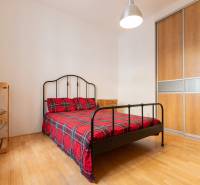 Schlafzimmer in einer 4-Zimmer-Wohnung mit einem Metallbett, einem Kleiderschrank und einem Boden in Holzoptik.