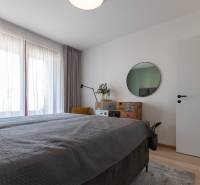 Schlafzimmer mit Bett, Spiegel und Kommode, auf einem Boden mit Holzdekor in einer 2-Zimmer-Wohnung.