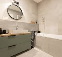 Badezimmer in einer 2-Zimmer-Wohnung mit Badewanne, Waschbecken und rundem Spiegel an der Wand.