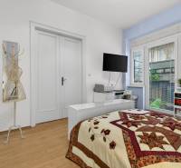 Schlafzimmer in einer 3-Zimmer-Wohnung mit Bett, Regalen und Boden mit Holzdekor.