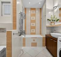 Badezimmer mit Badewanne, Waschmaschine, Waschbecken und dekorativen Fliesen in einer 3-Zimmer-Wohnung.