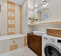 Badezimmer in einer 3-Zimmer-Wohnung mit Badewanne, Waschmaschine und braunen Fliesen.