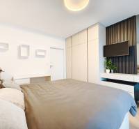 Schlafzimmer in einer 2-Zimmer-Wohnung mit Bett, Kleiderschrank und Fernseher an der Wand.