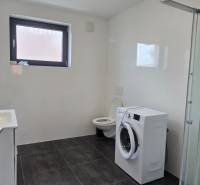 Badezimmer in einer 3-Zimmer-Wohnung mit Duschkabine, Waschmaschine und schwarzen Fliesen.