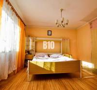 Ein Schlafzimmer in einem Einfamilienhaus mit einem Doppelbett, orangefarbenen Vorhängen und einem Boden in Holzoptik.