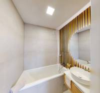 Badezimmer mit Badewanne und Waschbecken, Holzverkleidung an der Wand.