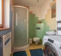 Badezimmer in einem Einfamilienhaus mit Waschmaschine, Duschkabine und bunten Fliesen.