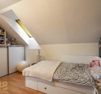 Dachzimmer mit Bett, Regalen, Dekorationen und Holzboden in einem Einfamilienhaus.