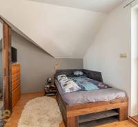 Ein Schlafzimmer in einem Einfamilienhaus mit einem gemütlichen Bett, einer schrägen Decke und einem Boden in Holzoptik.