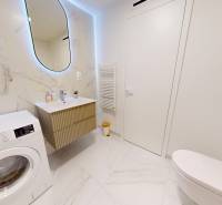 Badezimmer in einer Einzimmerwohnung mit Waschmaschine, Waschbecken und Keramikfliesen.
