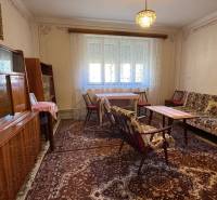 Wohnzimmer in einem Einfamilienhaus mit Teppich, Möbeln und Kronleuchter, Vorhänge an den Fenstern.