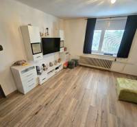 Wohnzimmer in einem Einfamilienhaus mit Fernseher, weißen Möbeln und einem Boden in Holzoptik.