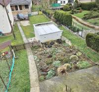 Ein Einfamilienhaus in Horné Ozorovce, Bánovce nad Bebravou, zeigt einen Garten mit einem Blumenbeet und einer Garage.