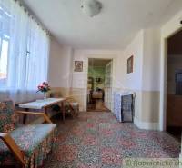 Innenraum eines Einfamilienhauses mit einer Sitzgelegenheit mit Blumenmuster und großen Fenstern, die Licht hereinlassen.