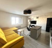 Wohnzimmer mit großem gelbem Sofa, Kücheninsel und Fernseher in einer 2-Zimmer-Wohnung.