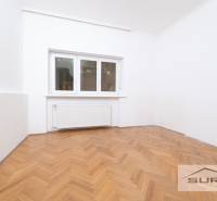 Ein Zimmer in einer 4-Zimmer-Wohnung mit weißen Wänden und einem Boden in Holzoptik.