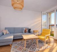 Wohnzimmer mit Sofa, gelbem Sessel, Teppich und Boden mit Holzdekor in einer 3-Zimmer-Wohnung.