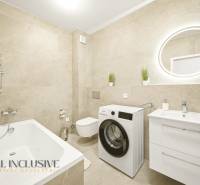 Badezimmer mit Dusche, Waschmaschine und Waschbecken in einer 4-Zimmer-Wohnung mit beigen Fliesen.