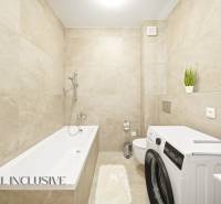 Ein Badezimmer mit hellen Fliesen, einer Badewanne, einer Waschmaschine und dekorativen Pflanzen in einer 4-Zimmer-Wohnung.