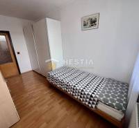 Ein Zimmer in einer 2-Zimmer-Wohnung mit einem Bett, einem Kleiderschrank und einem Boden in Holzoptik.