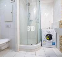 Badezimmer in einer Einzimmerwohnung mit Waschmaschine, Duschkabine und Keramikfliesen.