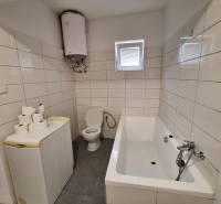 Badezimmer in einem Einfamilienhaus mit Badewanne, Waschmaschine, Boiler und Toilette.