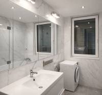 Badezimmer in einer 2-Zimmer-Wohnung mit Badewanne, Waschbecken und Waschmaschine, Fliesen in Marmoroptik.