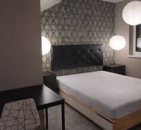 Schlafzimmer mit Bett, Abendbeleuchtung, Tisch und Stuhl in einer Zweizimmerwohnung.