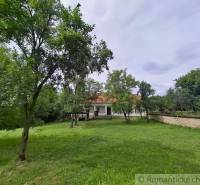 Ein Einfamilienhaus in Dobroč mit einem weitläufigen Garten, umgeben von Bäumen und einer Steinmauer.