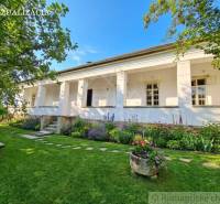 Ein Einfamilienhaus in Dobroč mit Garten und Blumenbeeten, umgeben von Bäumen und einer Bank.