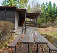 Eine Hütte mit Terrasse und Tisch auf den Erholungsgrundstücken in Holčíkovce, umgeben von Wald.