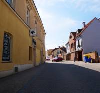 Eine Straße in Trnava mit Gastronomiebetrieben, gelbe und Backsteingebäude, geparktes Auto.