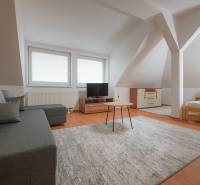 Dachzimmer in einer 2-Zimmer-Wohnung mit Sofa, Teppich und Holzboden.