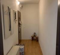 Ein schmaler Flur mit weißen Wänden, einem Boden in Holzoptik und minimalistischen Möbeln.