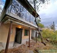Ein Ferienhaus in Kamenín mit einem verglasten Balkon, umgeben von Natur und einem überwucherten Hof.