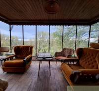 Interieur einer Hütte mit bequemen Sesseln und Blick auf Bäume durch große Fenster.