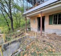 Eine Hütte in Kamenín, umgeben von Bäumen und einem Geländer, mit einem Eingang auf einer Betonterrasse.