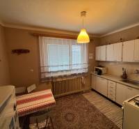 Küche in einem Einfamilienhaus mit weißen Schränken, gemustertem Teppich und Esstisch.