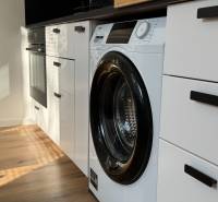 Küche in einer Einzimmerwohnung mit eingebauter Waschmaschine und Boden mit Holzdekor.