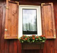 Ein Fenster eines Einfamilienhauses in Bohdanovce nad Trnavou mit Fensterläden und einem Blumenkasten mit roten Blumen.