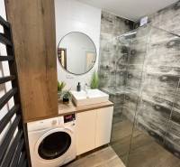 Badezimmer mit Duschkabine, Waschbecken, Waschmaschine und Boden mit Holzdekor in einer 2-Zimmer-Wohnung.