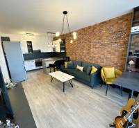 Wohnbereich einer 2-Zimmer-Wohnung mit Ziegelwand, Holzboden und Küchenzeile.